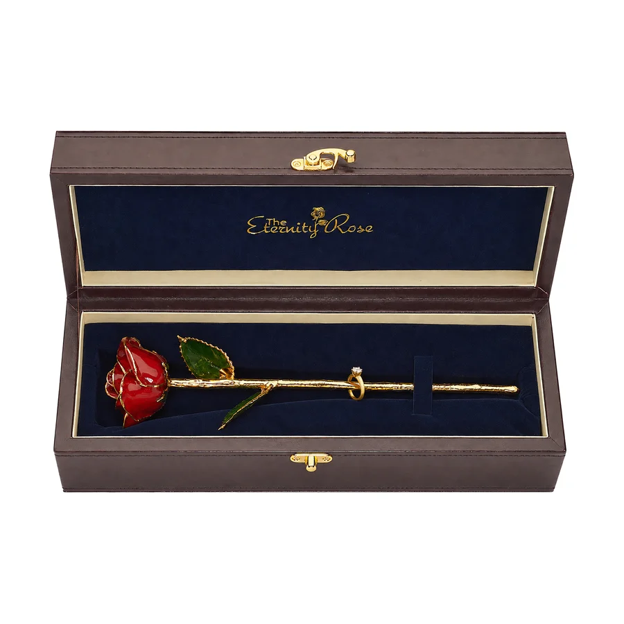 A red glazed natural rose with gold trim and an engagement ring on its stem, in its open leather presentation case