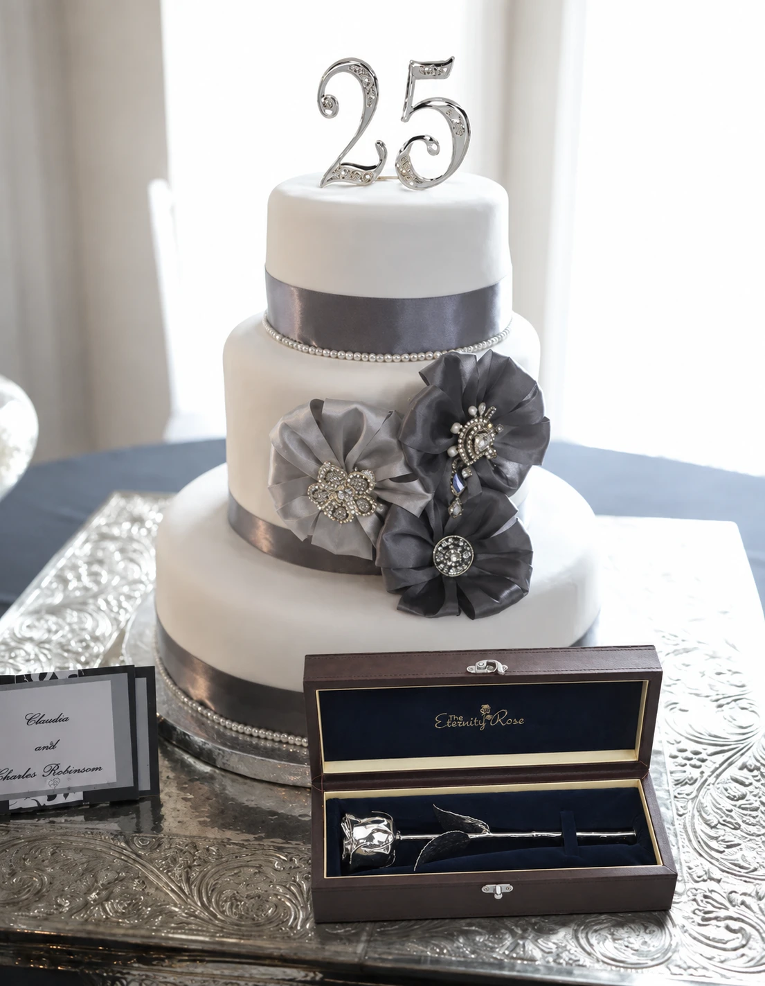 A silver twenty-five cake topper on a silver anniversary cake with an Eternity Rose presentation case